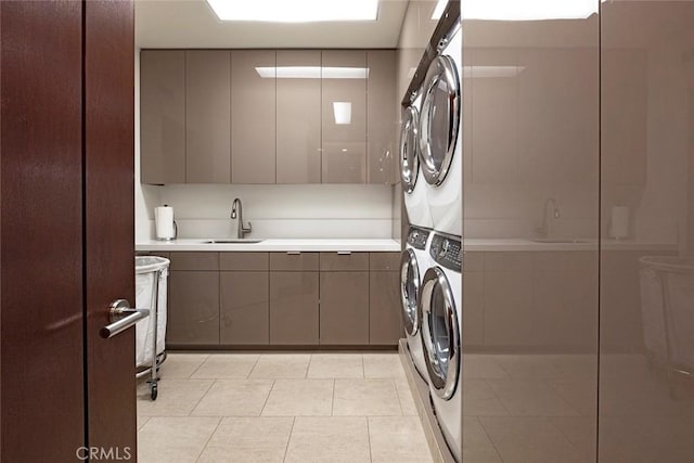 laundry room with light tile patterned flooring, cabinets, stacked washing maching and dryer, and sink