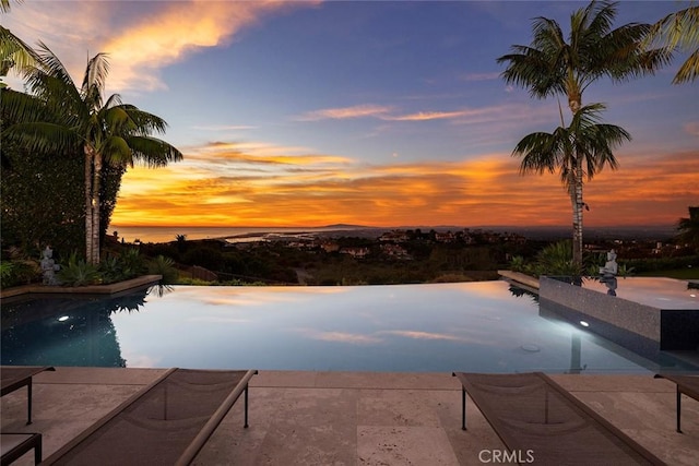 pool at dusk with a patio and a water view