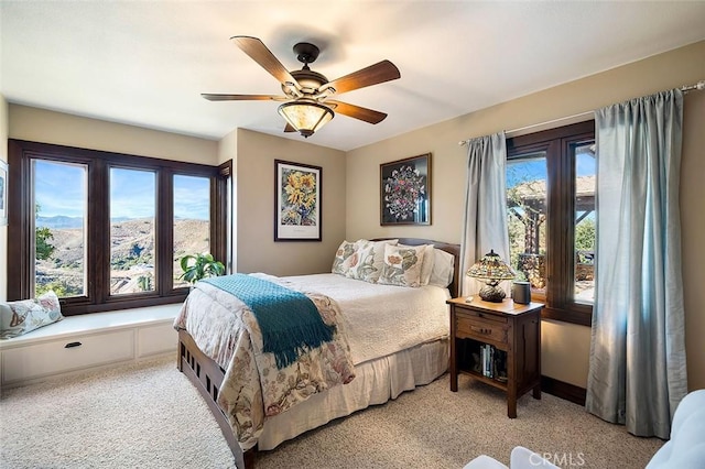 bedroom featuring ceiling fan, light colored carpet, a mountain view, and multiple windows