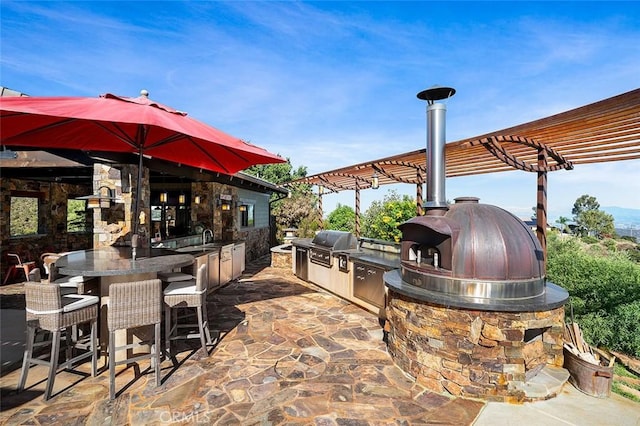 view of patio / terrace featuring an outdoor kitchen, a pergola, a grill, and a wet bar