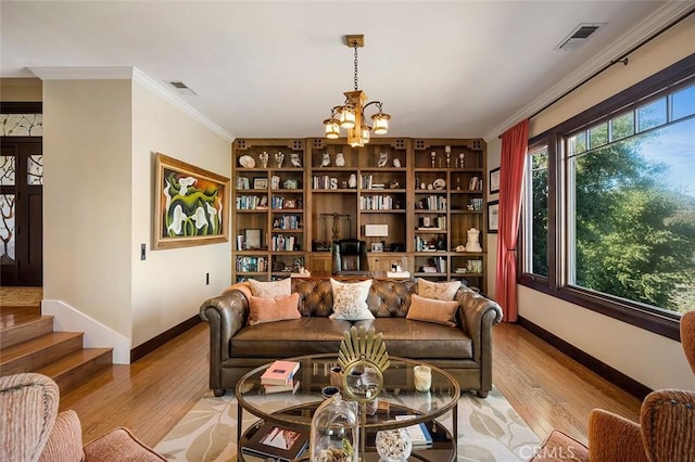 living room featuring light wood-type flooring, built in shelves, crown molding, and a notable chandelier