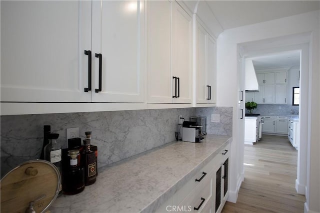 kitchen featuring tasteful backsplash, high end stove, light hardwood / wood-style flooring, light stone countertops, and white cabinets