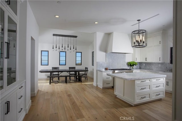 kitchen featuring premium range hood, white cabinetry, a center island, and hanging light fixtures