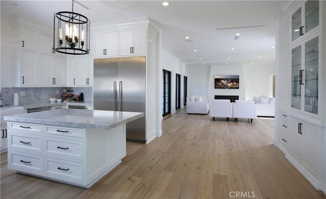 kitchen featuring backsplash, pendant lighting, light wood-type flooring, stainless steel built in fridge, and white cabinets