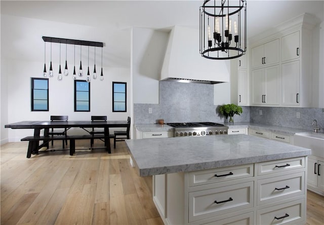 kitchen with a center island, range, white cabinetry, hanging light fixtures, and custom range hood