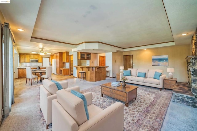 living room featuring ceiling fan, light colored carpet, and a tray ceiling