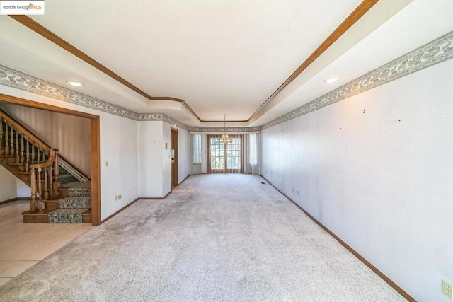 carpeted spare room featuring a raised ceiling, an inviting chandelier, and crown molding