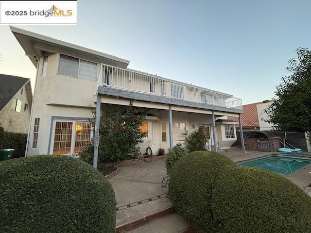 back of property with a fenced in pool, a balcony, and a patio