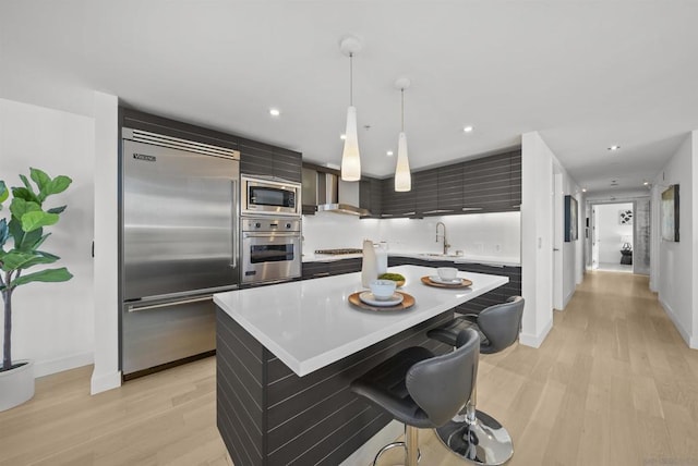 kitchen with a kitchen bar, built in appliances, light hardwood / wood-style floors, and a center island