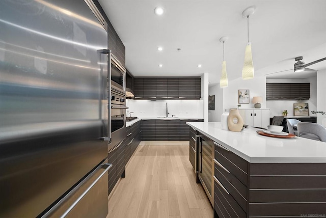 kitchen featuring decorative light fixtures, ceiling fan, a kitchen island, light hardwood / wood-style flooring, and appliances with stainless steel finishes