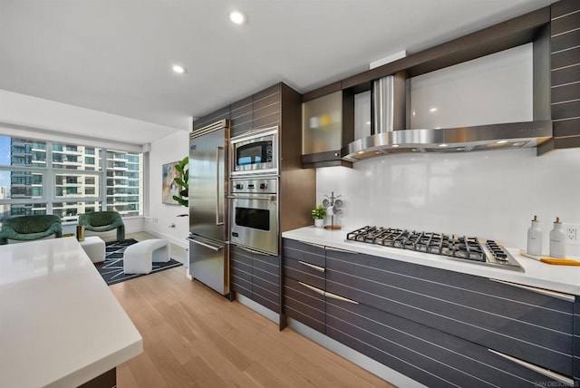 kitchen featuring wall chimney range hood, light hardwood / wood-style flooring, and built in appliances