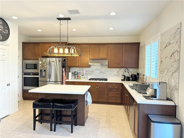 kitchen featuring a kitchen breakfast bar, pendant lighting, appliances with stainless steel finishes, sink, and backsplash