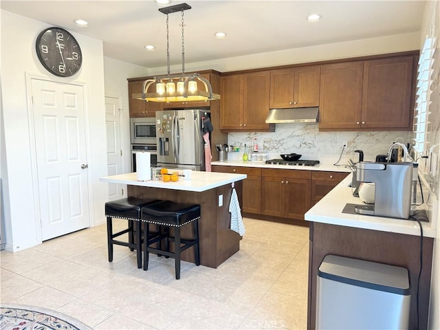 kitchen featuring pendant lighting, appliances with stainless steel finishes, a kitchen island, a kitchen bar, and backsplash