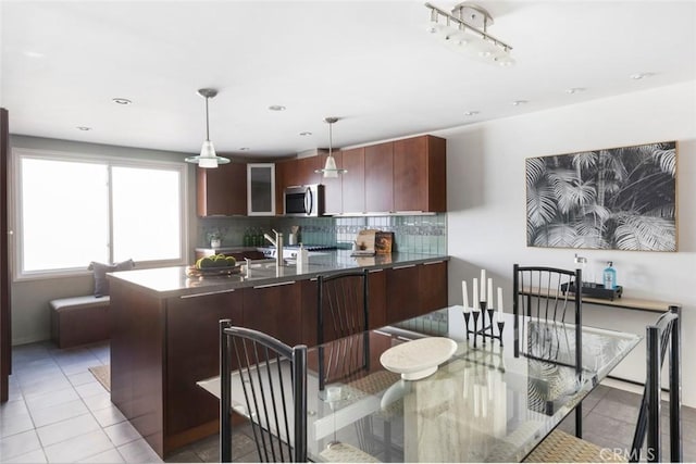 kitchen with light tile patterned flooring, decorative backsplash, pendant lighting, and dark brown cabinetry