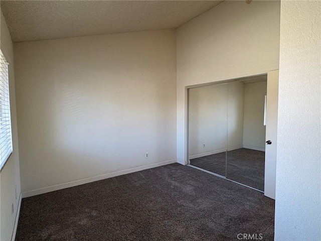 unfurnished bedroom with lofted ceiling, a closet, dark carpet, and a textured ceiling