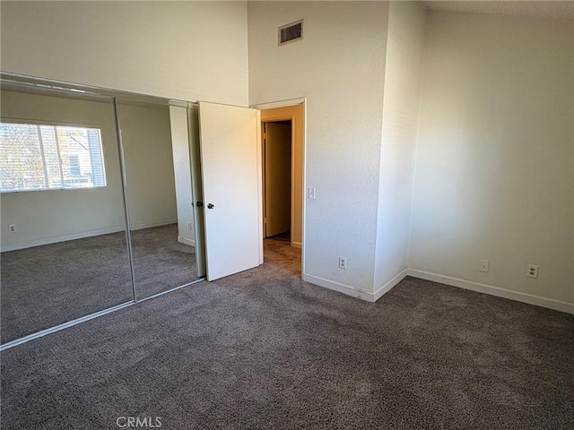 unfurnished bedroom featuring dark carpet, a closet, and a towering ceiling