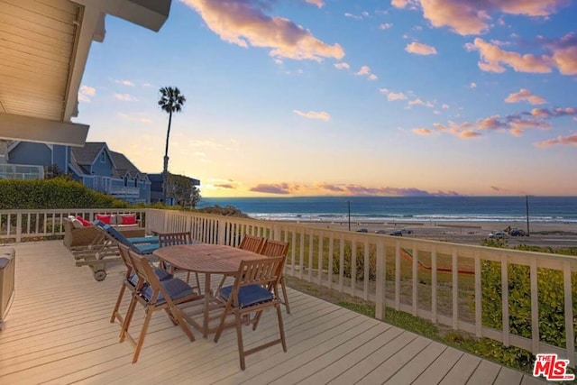 deck at dusk featuring a beach view and a water view