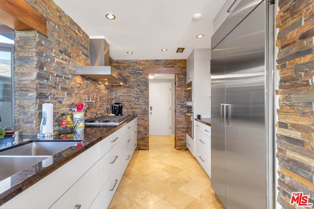 kitchen featuring white cabinets, ventilation hood, stainless steel appliances, and dark stone countertops