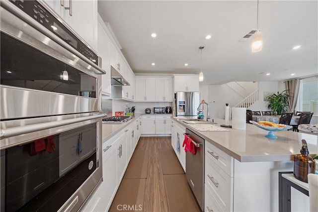 kitchen featuring appliances with stainless steel finishes, white cabinetry, sink, hanging light fixtures, and a kitchen island with sink