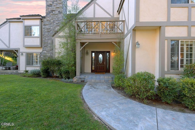 exterior entry at dusk with a lawn and a balcony