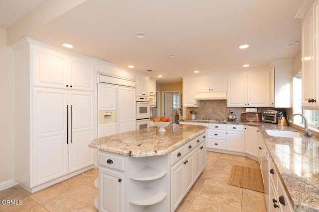 kitchen with light stone countertops, sink, white cabinetry, and a kitchen island