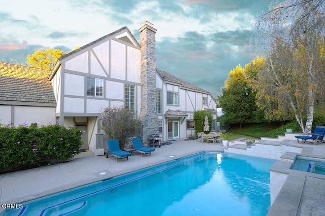 rear view of house featuring a swimming pool with hot tub and a patio