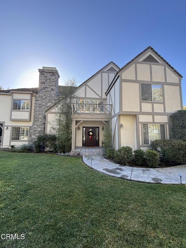 tudor home with a balcony and a front yard