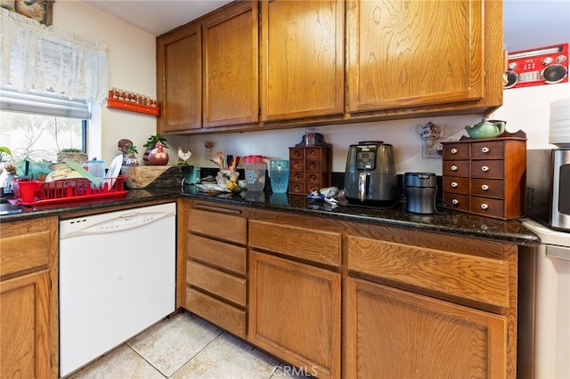 kitchen featuring light tile patterned floors, dark stone countertops, and white dishwasher