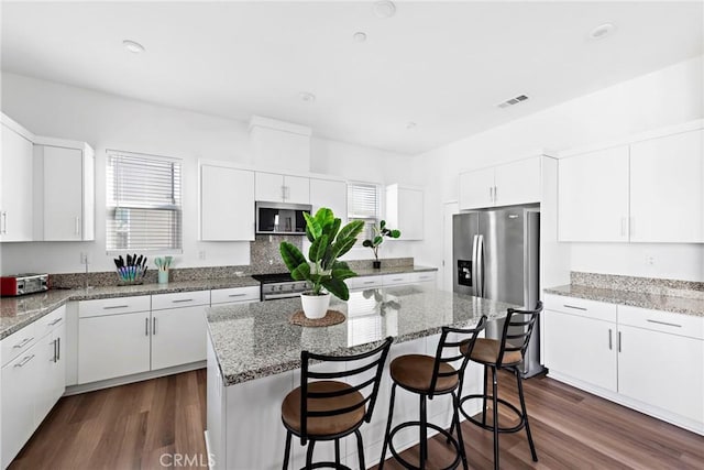 kitchen with a center island, light stone countertops, a breakfast bar area, stainless steel appliances, and white cabinets