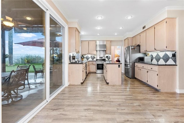 kitchen with appliances with stainless steel finishes, wall chimney range hood, light brown cabinets, and a kitchen island