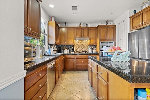 kitchen with appliances with stainless steel finishes, a kitchen island, sink, backsplash, and light tile patterned floors