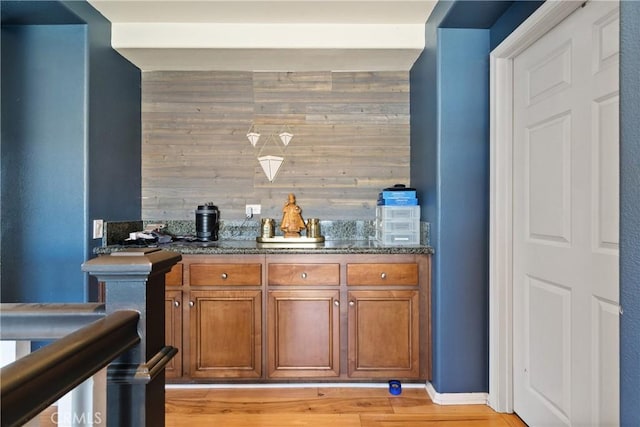 bar with dark stone counters, wooden walls, and light hardwood / wood-style floors