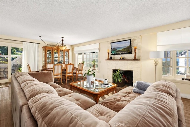 living room featuring dark wood-type flooring, a stone fireplace, and a textured ceiling