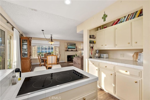 kitchen featuring black electric stovetop, pendant lighting, light wood-type flooring, a textured ceiling, and tile counters