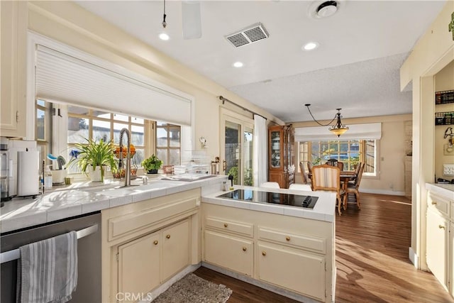 kitchen featuring dishwasher, black electric stovetop, sink, tile counters, and cream cabinetry