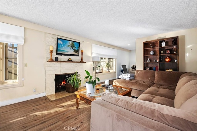 living room featuring a stone fireplace, a textured ceiling, and hardwood / wood-style flooring