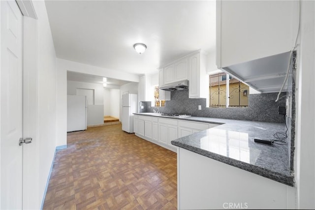 kitchen with kitchen peninsula, white refrigerator, white cabinetry, and parquet flooring