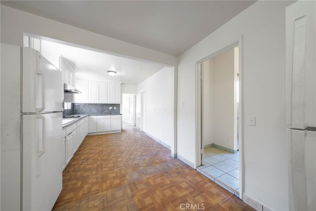 kitchen featuring light parquet flooring, backsplash, white fridge, and white cabinetry