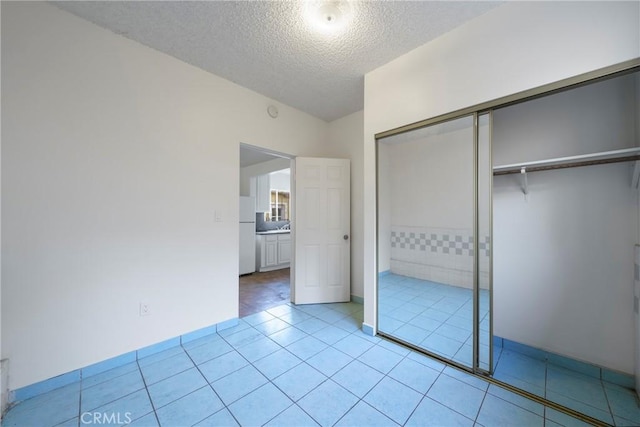 unfurnished bedroom with light tile patterned floors, a closet, white refrigerator, and a textured ceiling