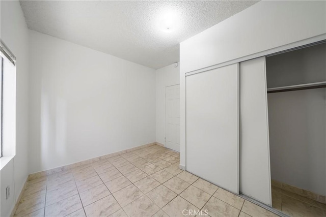 unfurnished bedroom with a textured ceiling, light tile patterned floors, and a closet