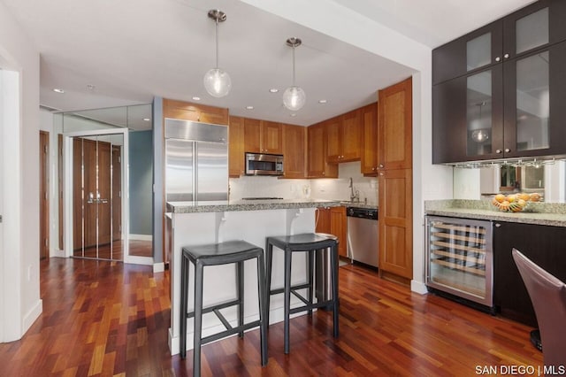 kitchen with stainless steel appliances, dark hardwood / wood-style flooring, wine cooler, pendant lighting, and light stone counters