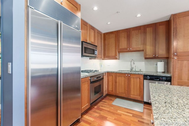 kitchen featuring appliances with stainless steel finishes, sink, light stone counters, and light hardwood / wood-style floors