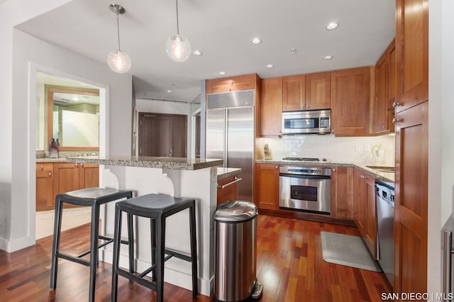 kitchen with appliances with stainless steel finishes, backsplash, pendant lighting, a breakfast bar, and a center island