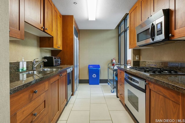 kitchen featuring light tile patterned floors, appliances with stainless steel finishes, dark stone counters, a textured ceiling, and sink