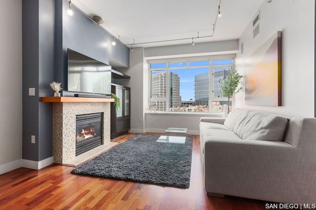 living room featuring a tiled fireplace, track lighting, and hardwood / wood-style flooring