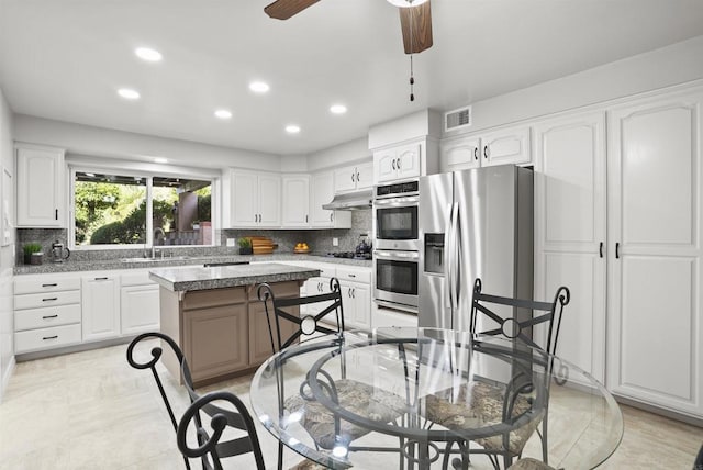 kitchen featuring white cabinetry, stainless steel appliances, a center island, sink, and light stone counters