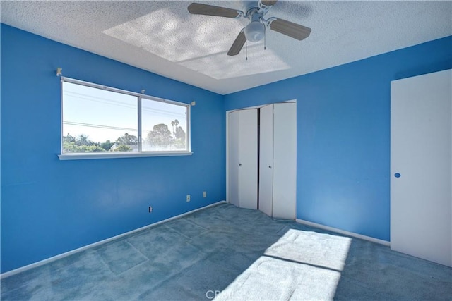 unfurnished bedroom featuring ceiling fan, a textured ceiling, a closet, and carpet flooring