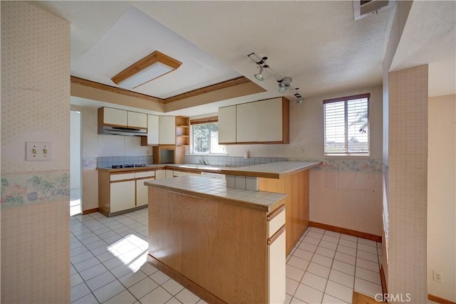 kitchen with gas stovetop, tile counters, a wealth of natural light, and kitchen peninsula