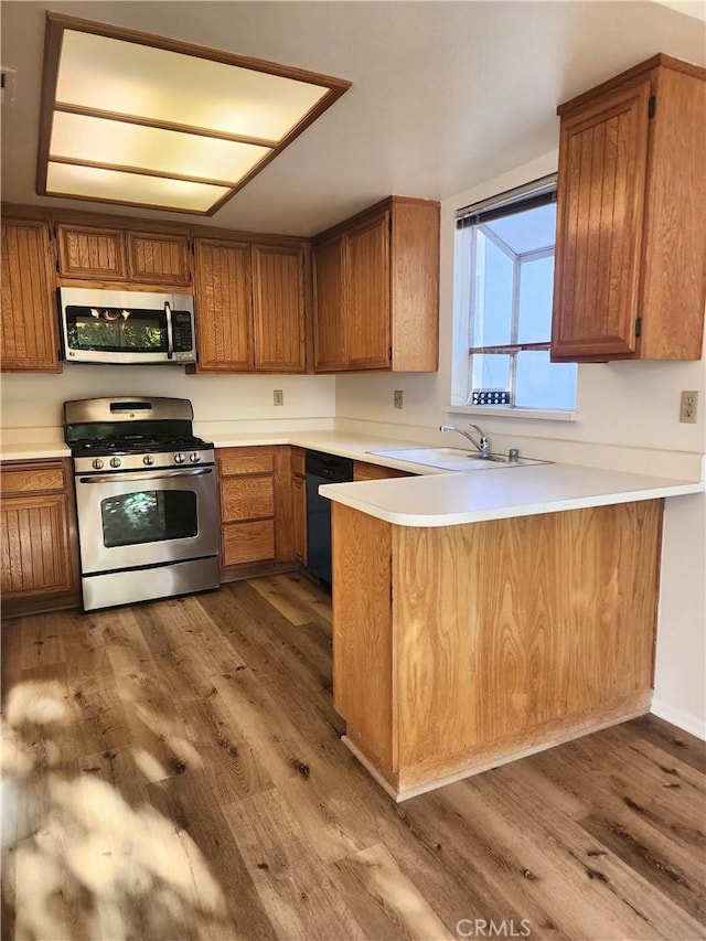 kitchen featuring dark wood-type flooring, appliances with stainless steel finishes, kitchen peninsula, and sink