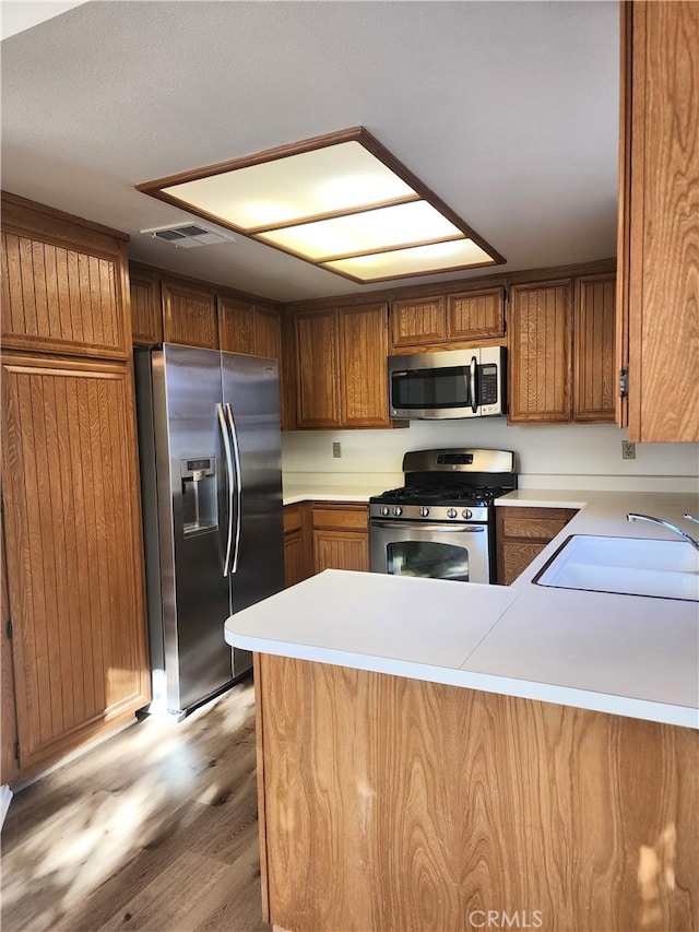 kitchen with stainless steel appliances, light hardwood / wood-style floors, kitchen peninsula, and sink